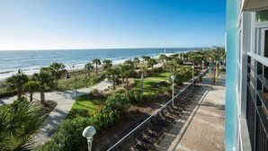 En balkon med udsigt over stranden og havet, en belagt sti og en række stole.