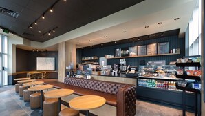En moderne café med en lang disk, flere siddepladser inklusive en bænk og runde borde, samt en menutavle.