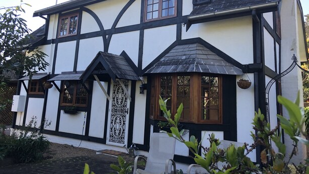 A two-story Tudor-style house with black timber framing, white walls, and a steeply pitched roof.