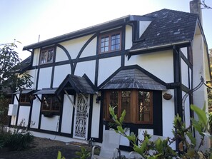 Una casa de estilo Tudor de dos plantas con entramado de madera negra, paredes blancas y un techo empinado.