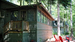 A cabin with a wooden deck, large windows, and potted plants. - Historic Glen Lake Cottage with Private Waterfront Access (Glen Arbor)