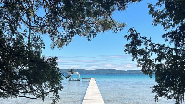 A wooden pier extending into clear water, surrounded by trees. - Historic Glen Lake Cottage with Private Waterfront Access (Glen Arbor)