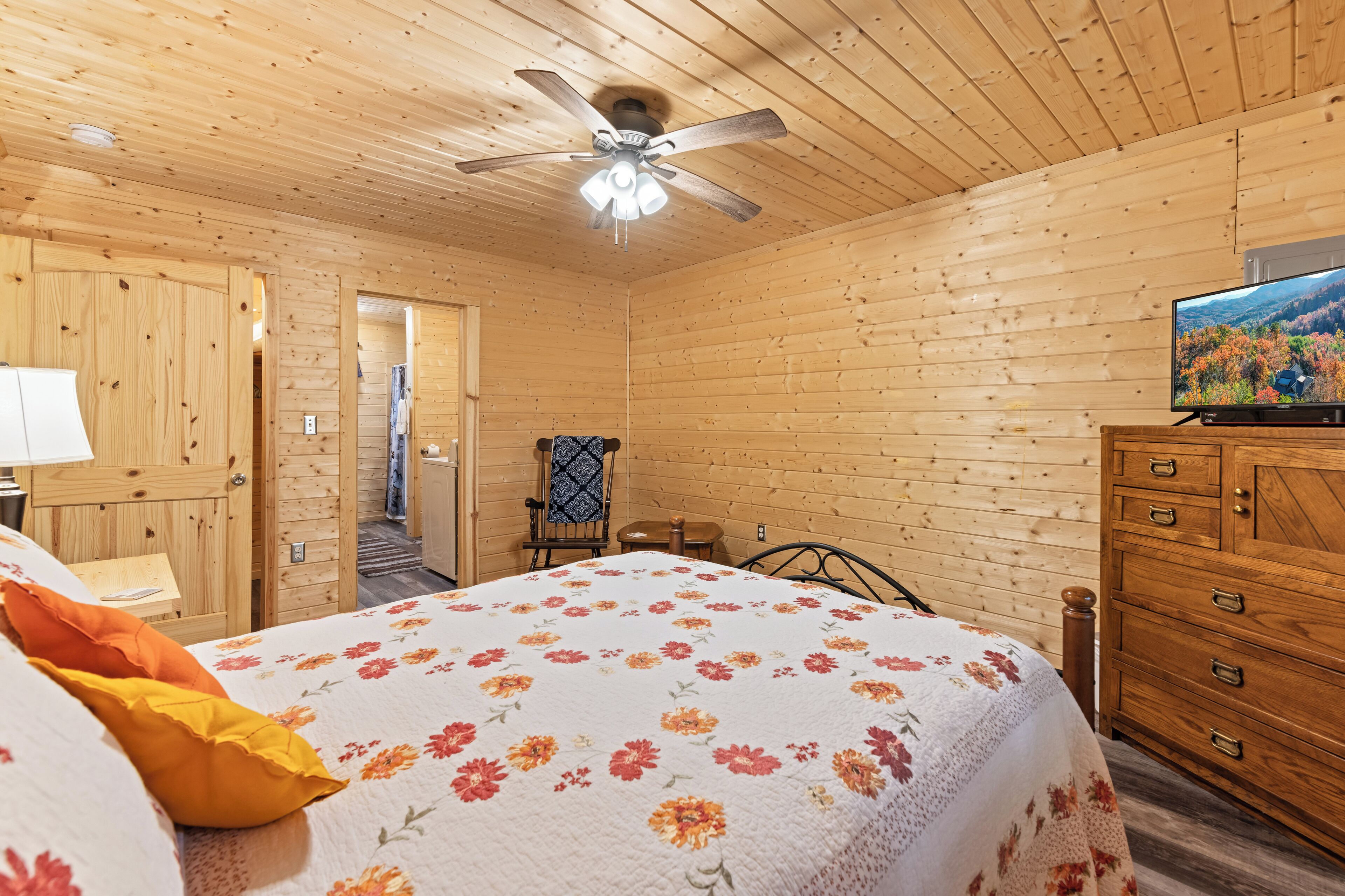 A wooden cabin bedroom with a bed, dresser, and ceiling fan.