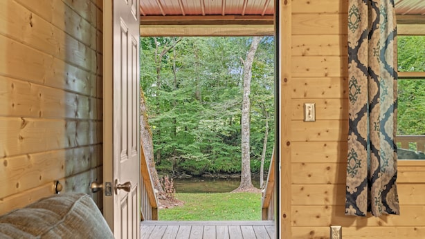 A wooden cabin with a door leading to a deck overlooking a forested area.