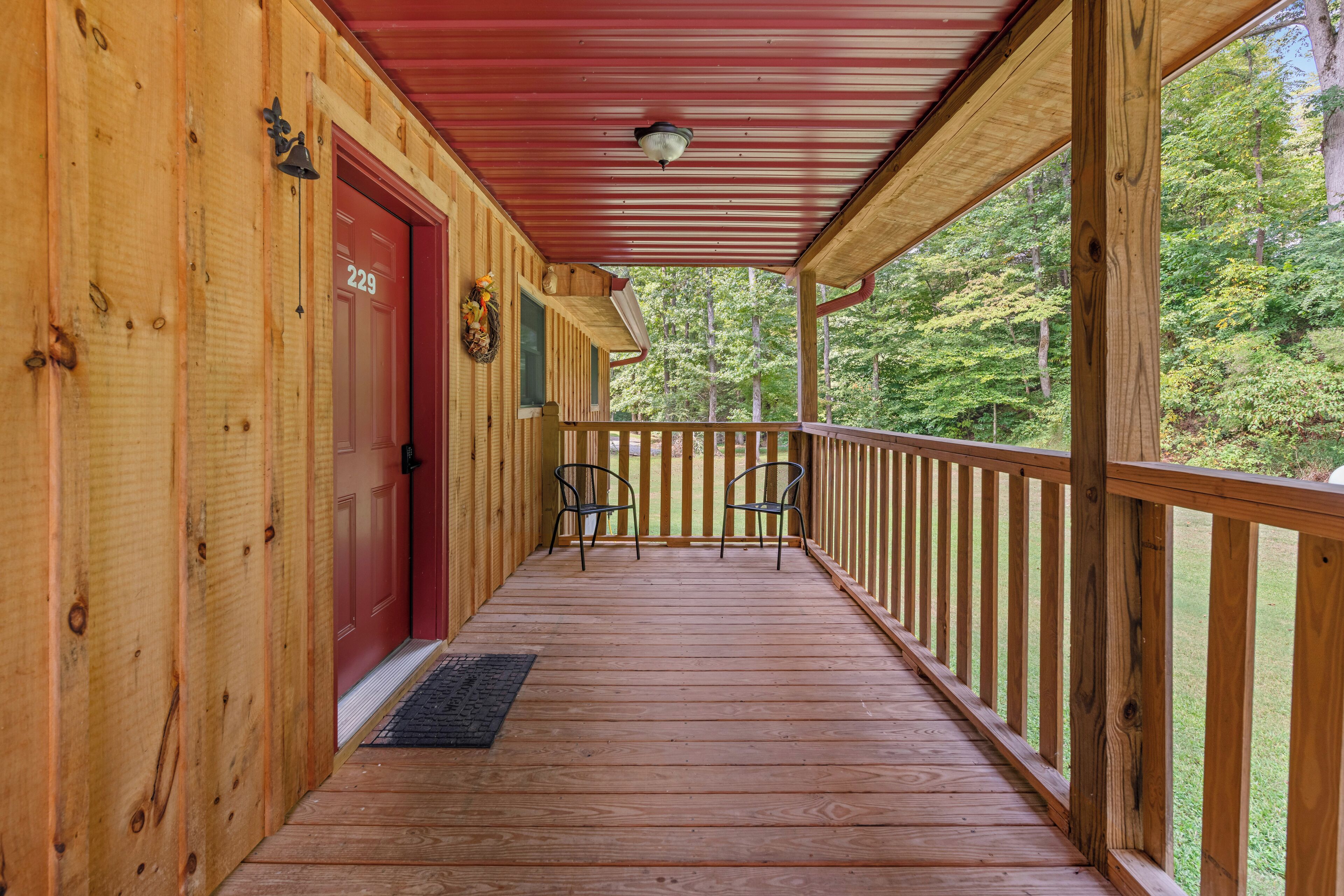 A wooden porch with a red door, two chairs, and a view of a forest.