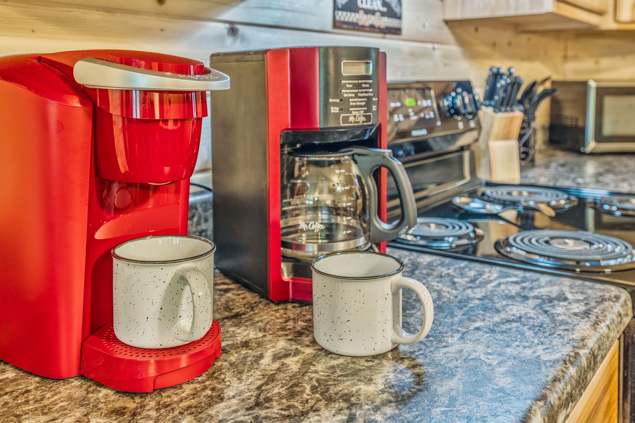 Une machine à café rouge et deux tasses blanches sur un plan de travail de cuisine.