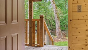 A wooden porch with a sign reading "The Porch Sit & Relax" leading to a forested area with a river.