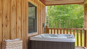 A wooden cabin with a hot tub on a deck, surrounded by trees.