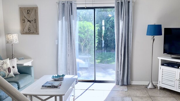 Ein Wohnzimmer mit einem weißen Sofa, einem Couchtisch, einem Fernseher, einem Deckenventilator und Blick durch eine Glastür.