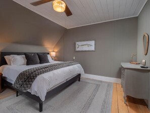 A bedroom with a bed, bedside tables, a nightstand, a ceiling fan, a wall-mounted light, and a framed fish illustration.