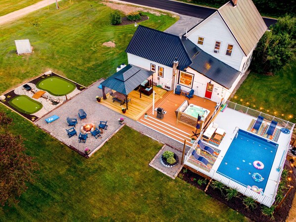 A house with a large deck, a hot tub, a swimming pool, and a small putting green.