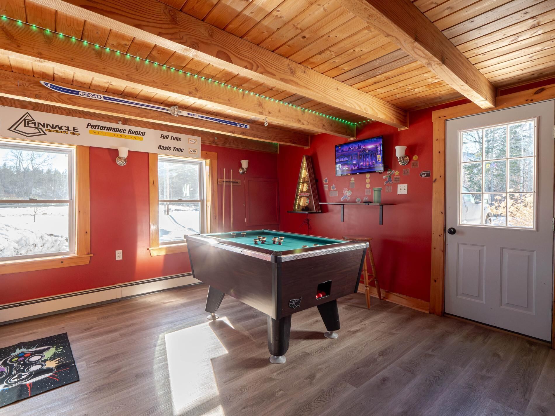A room with a pool table, a television, and a door with a view of a snowy landscape.