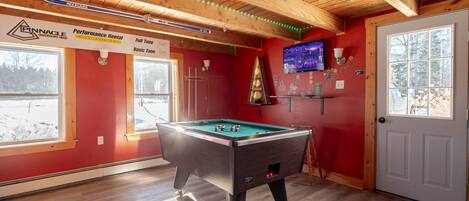 A room with a pool table, a television, and a door with a view of a snowy landscape.