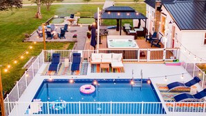En trädgård med en pool, solstolar, ett bubbelbad och en täckt uteplats.