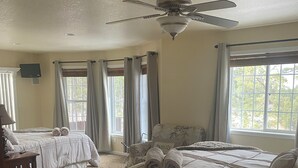 A bedroom with two beds, a ceiling fan, a TV, and large windows with curtains. - 7 Bedroom Spacious Lead Home with Game Room and Hot Tub (Lead)