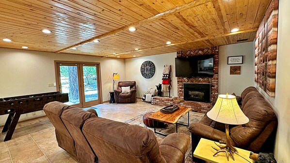 A cozy living room with a pool table, leather sofas, a fireplace, and a TV.