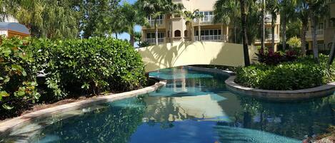 A pool surrounded by lush greenery and a multi-story building with balconies.