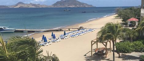 A beach with sun loungers and umbrellas, a wooden walkway, and a gazebo.
