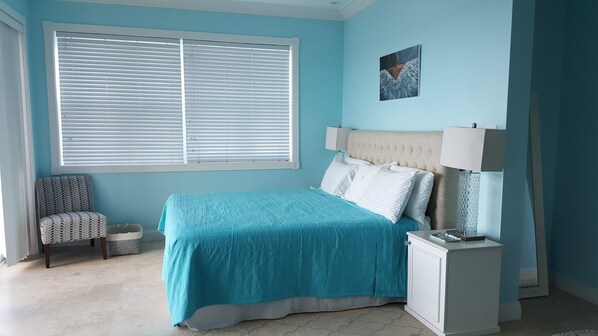 A bedroom with a bed, a chair, a nightstand, a lamp, and a painting on the wall.