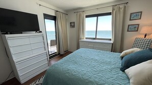 A bedroom with a bed, a dresser, a television, a window with curtains, and a view of the sea. - Horizon East 704 - Oceanfront in Garden City Beach, SC (Garden City)