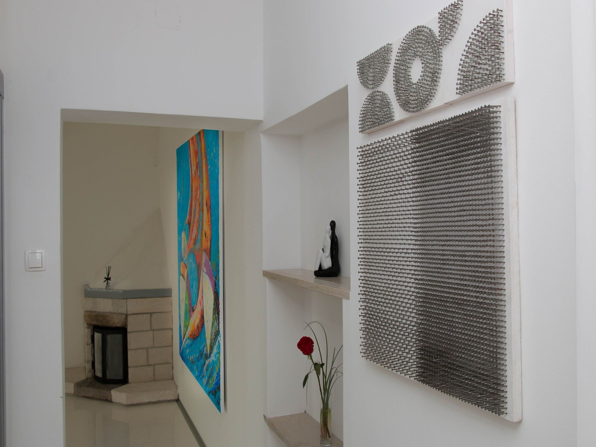 A hallway with a colorful abstract painting, a black sculpture, and a textured wall art piece.