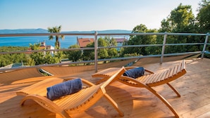 Eine Holzterrasse mit zwei Liegestühlen und einer Hängematte, mit Blick auf eine schöne Aussicht auf Meer und Hügel.