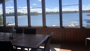 Eine Holzterrasse mit Tisch und Stühlen, große Fenster mit Blick auf einen See mit Booten und einem Steg.