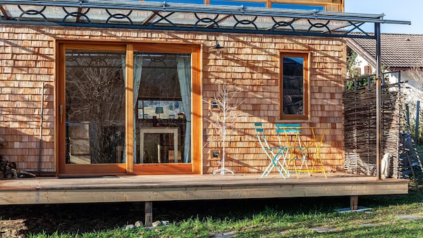 A wooden house with large glass doors, a small window, and a wooden deck. - Charming Tiny House “Loft Süd” with Mountain View, Wi-Fi, Terrace and Garden (Unterammergau)