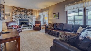 A cozy living room with a stone fireplace, leather sofas, and large windows offering a view. - Enjoy swimming/boating in the lake, Fall Foliage, Wine trail, Skiing and Hiking (Canandaigua)