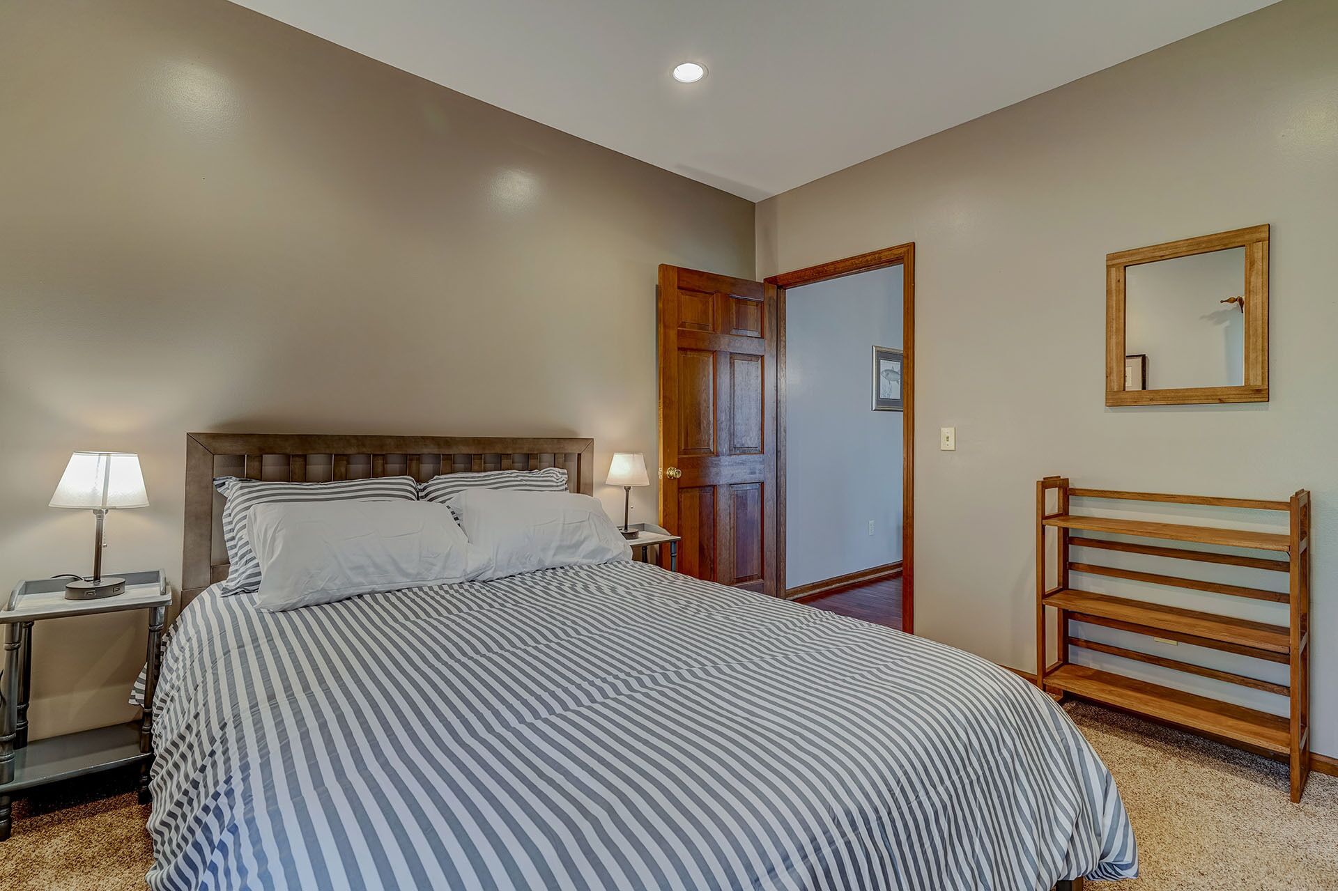 A bedroom with a bed, bedside lamps, a wooden headboard, a door, a mirror, and a wooden bench.