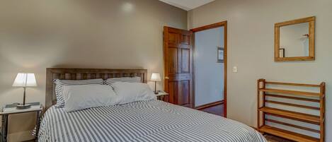 A bedroom with a bed, bedside lamps, a wooden headboard, a door, a mirror, and a wooden bench.
