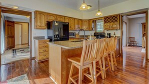 A spacious kitchen with wooden cabinets, a central island with bar stools, stainless steel appliances, and pendant lighting. - Enjoy swimming/boating in the lake, Fall Foliage, Wine trail, Skiing and Hiking (Canandaigua)