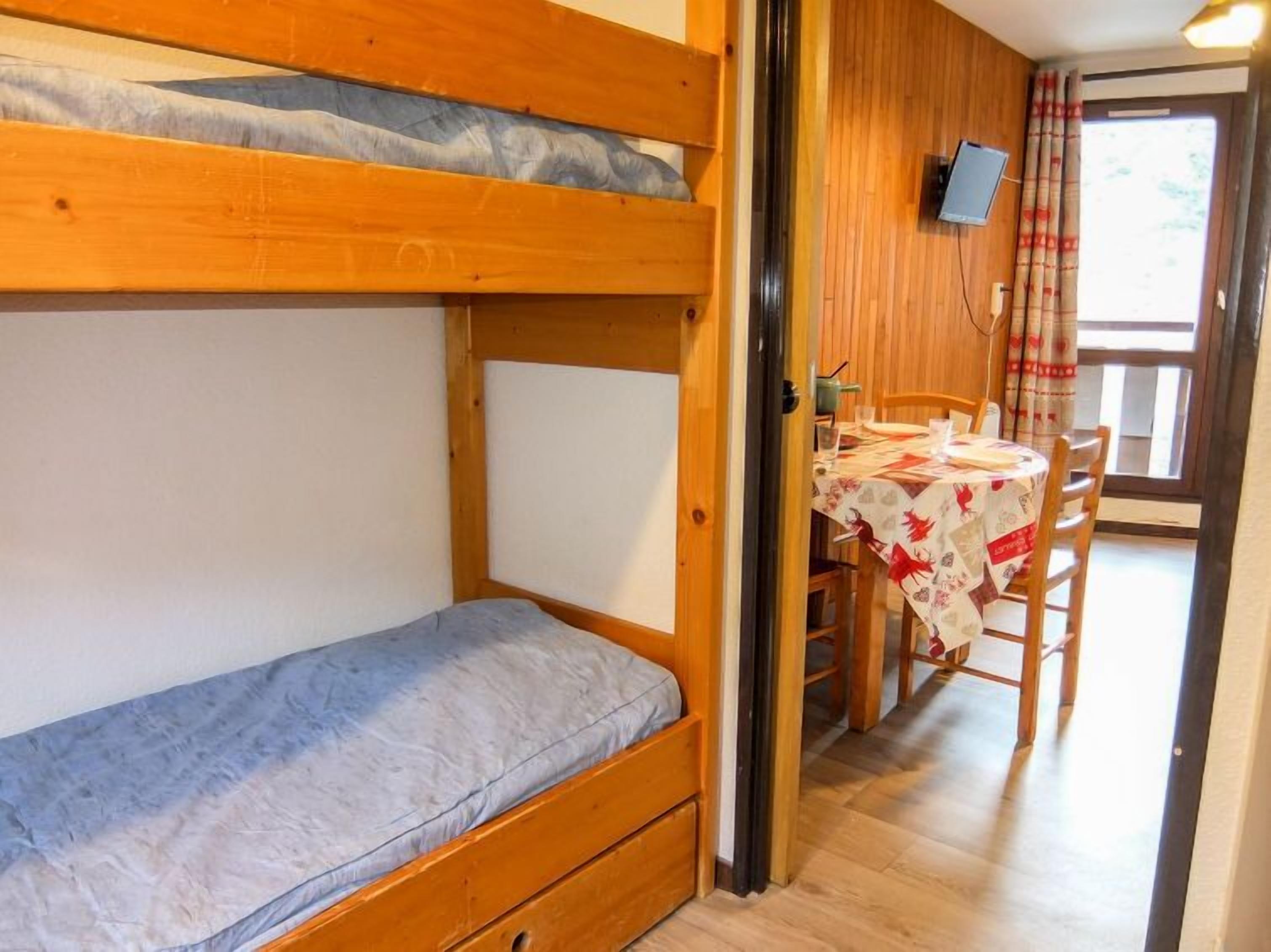 A bunk bed room with a wooden door leading to a dining area with a table and chairs.