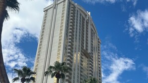 Un hotel alto y moderno con varios pisos y balcones, rodeado de palmeras bajo un cielo despejado.