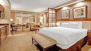 Habitación de hotel con una cama grande, un escritorio, sillas, un piano y vistas de la ciudad.