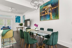 Zona pranzo moderna con tavolo in vetro, sedie imbottite verdi e un grande quadro astratto appeso al muro.
