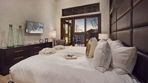 Une chambre à coucher moderne avec un grand lit, une commode, un téléviseur et une vue sur l’extérieur.