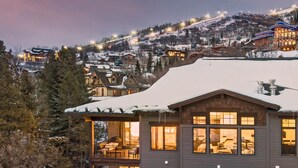 Un chalet dont le toit est recouvert de neige, doté de grandes fenêtres et offrant une vue sur une montagne enneigée.