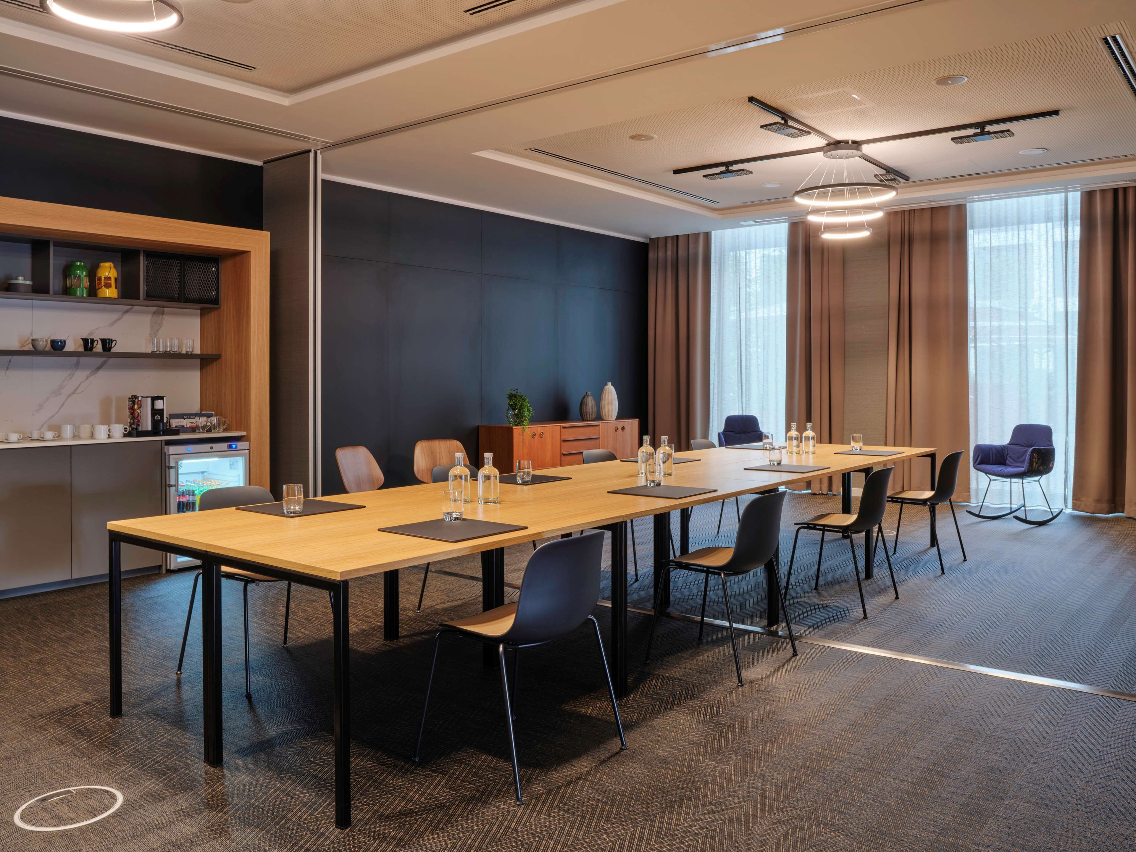 Une salle de conférence moderne équipée d’une longue table, de chaises et d’un coin cuisine.