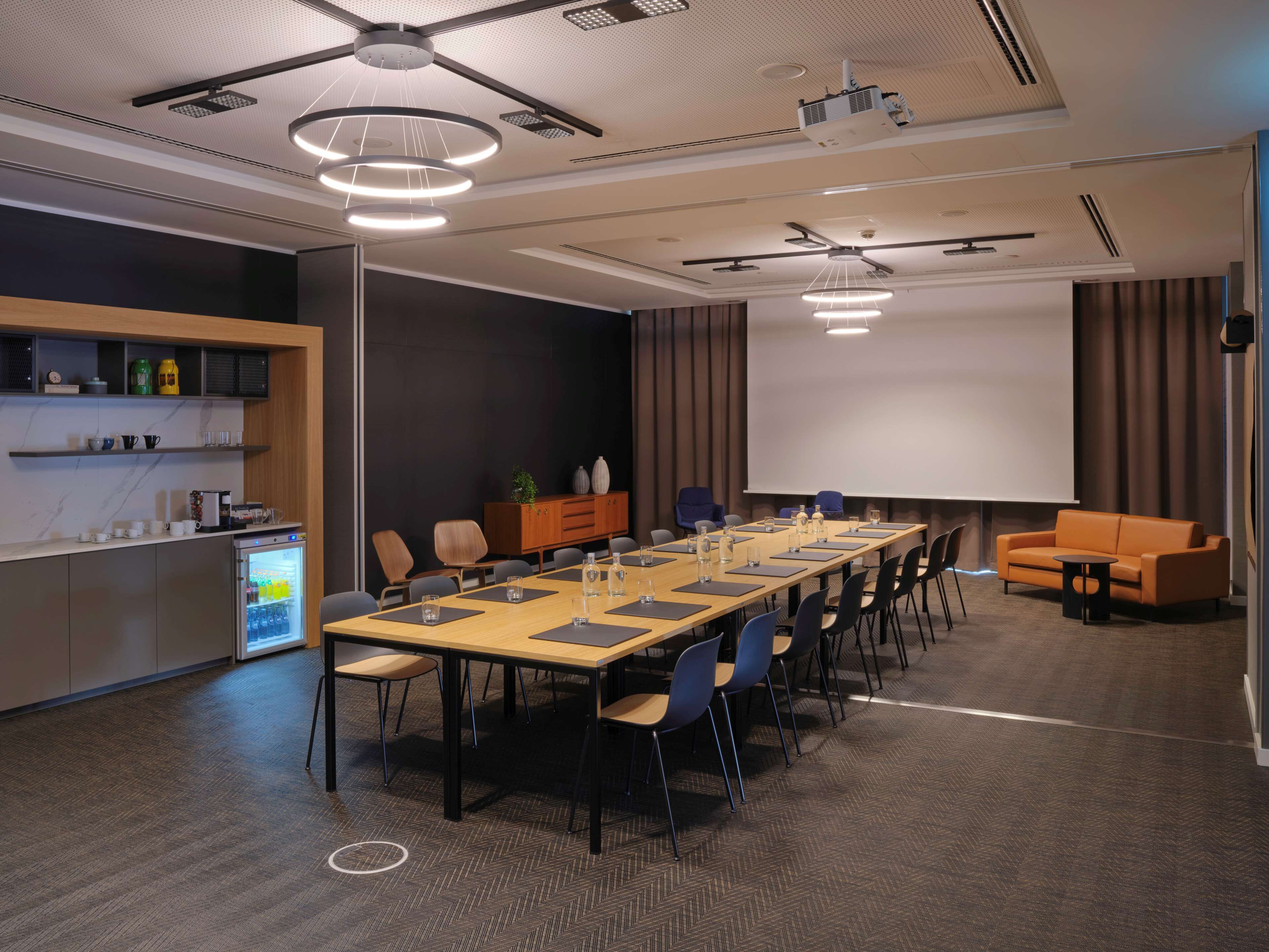A conference room with a long table, chairs, a projector screen, and a sofa.