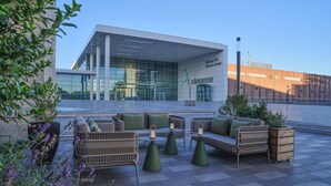 An outdoor seating area with wicker furniture and planters, in front of a building with glass windows and a sign reading "Entrance South". - Adina Apartment Hotel Cologne (Cologne)