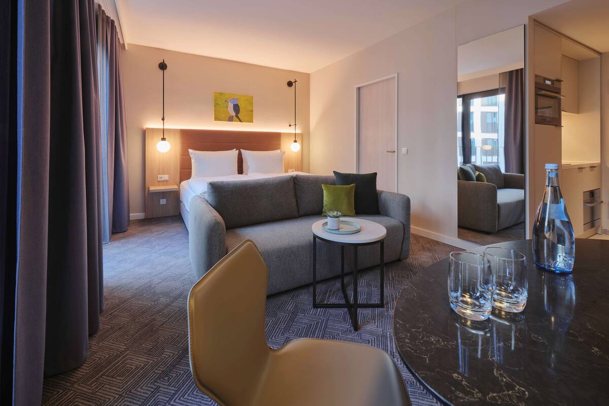 Una habitación de hotel moderna con cama, sofá y un área de comedor con mesa y sillas.