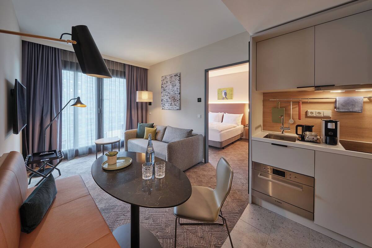 Una habitación de hotel moderna con sofá, una mesa de comedor, cama y kitchenette.