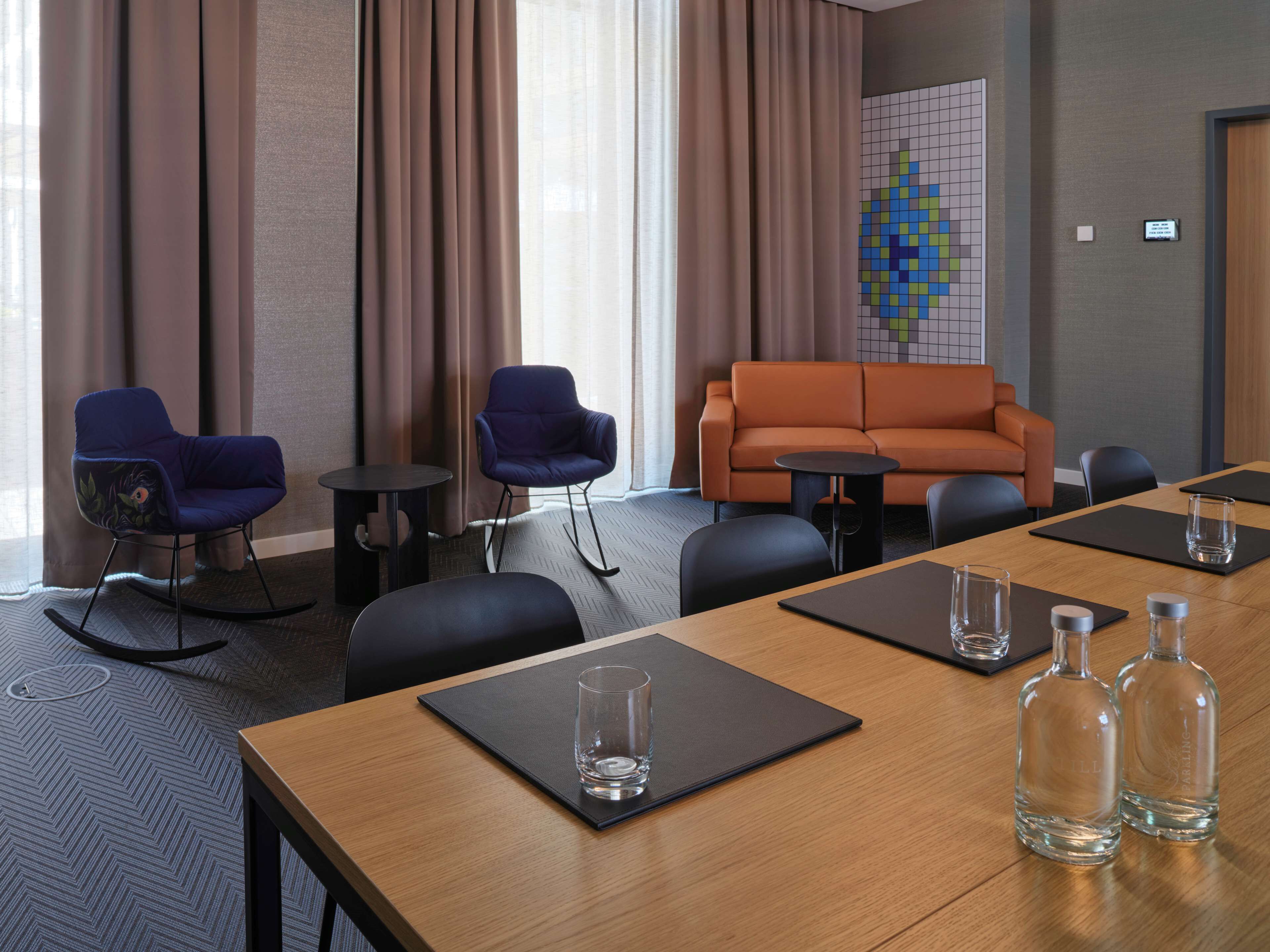 A conference room with a wooden table, two blue chairs, an orange sofa, and a small wall art piece.