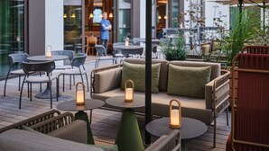 An outdoor seating area with wicker furniture, cushioned sofas, and round tables. - Adina Apartment Hotel Cologne (Cologne)