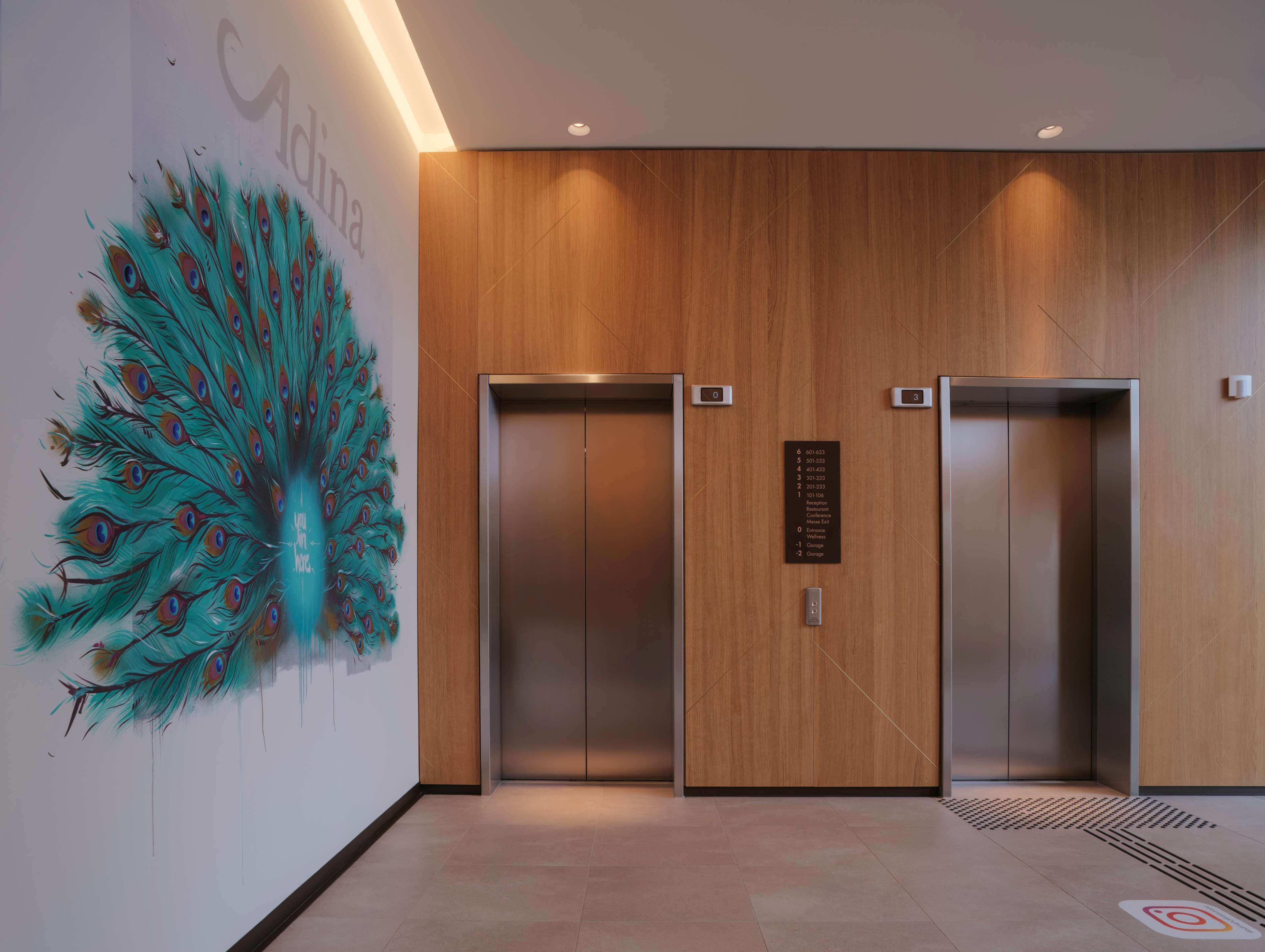 A modern elevator area with wooden paneling and a peacock feather mural.