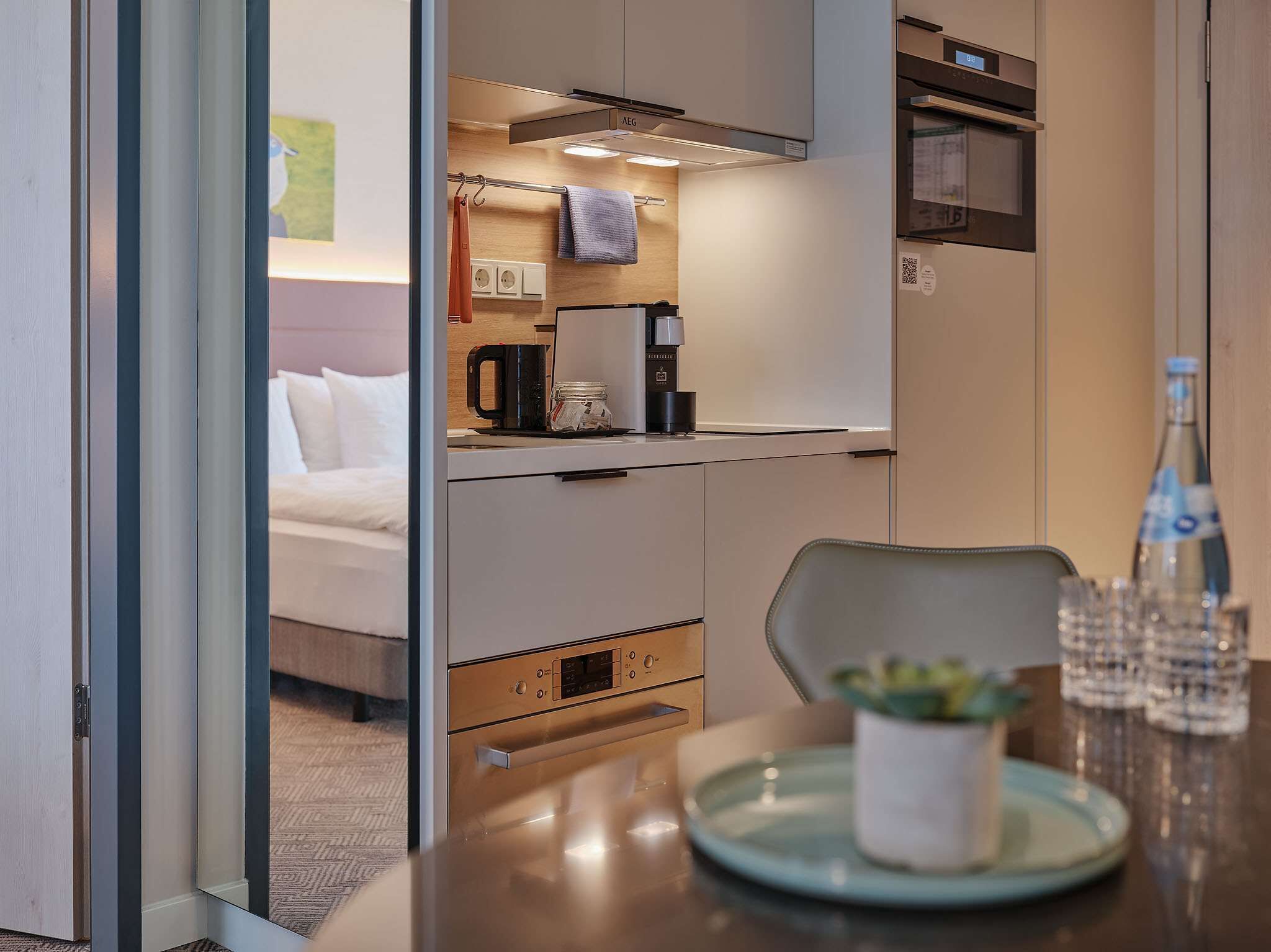 A compact hotel room with a kitchenette, a bed, and a dining area.