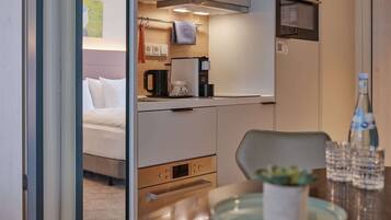 A compact hotel room with a kitchenette, a bed, and a dining area.