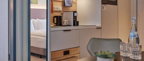 A compact hotel room with a kitchenette, a bed, and a dining area.