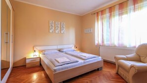 Ein Schlafzimmer mit einem Bett, Nachttischen, einem Sessel und einem Fenster mit Vorhängen.